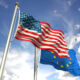 American and European Union flags waving against the sky.