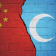 Cracked brick wall painted with a flag of China on the left and a flag of Uyghur on the right.