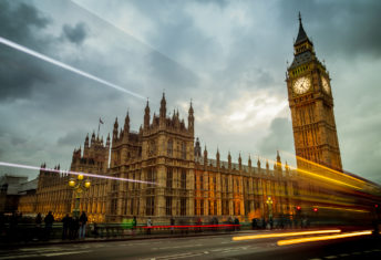 UK government advisers want clarity from ISSB amid GHG Protocol changes Big Ben and the Houses of Parliament in London, England. The building is lit up and set against a dramatic sky with cars and busses zooming by on Waterloo Bridge.