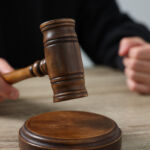 Exxon sues California over climate disclosure laws Judge with gavel sitting at wooden table against light grey background, closeup