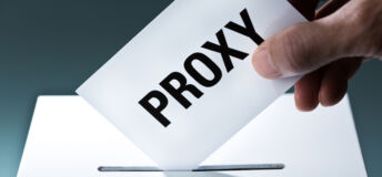 Voter's hand holding a proxy vote ballot, inserting the vote card into the ballot box.